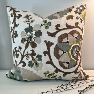 May include: Square decorative pillow with a floral pattern in shades of brown, green, gray, and beige on a white background. The pillow features a large-scale, stylized floral design, adding a touch of elegance to any room.