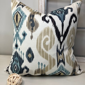 May include: A decorative throw pillow with a white background and a blue, brown, and black ikat pattern.