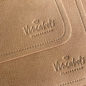 May include: Close-up of three brown leather placemats with the text "Vincabel's Playground" embossed on each.