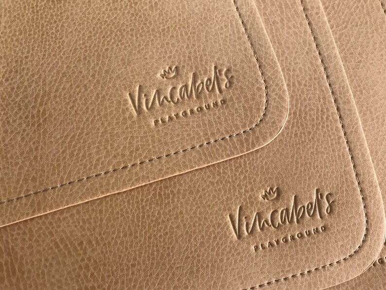 May include: Close-up of three brown leather placemats with the text "Vincabel's Playground" embossed on each.