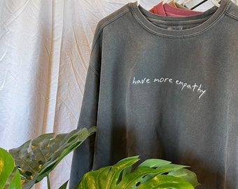May include: A dark gray sweatshirt with the phrase "have more empathy" embroidered in white on the front.