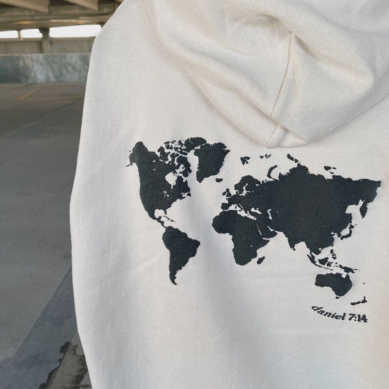 May include: A cream-colored hoodie with a black outline of the world map printed on the back. The text "daniel 7:14" is printed below the map.