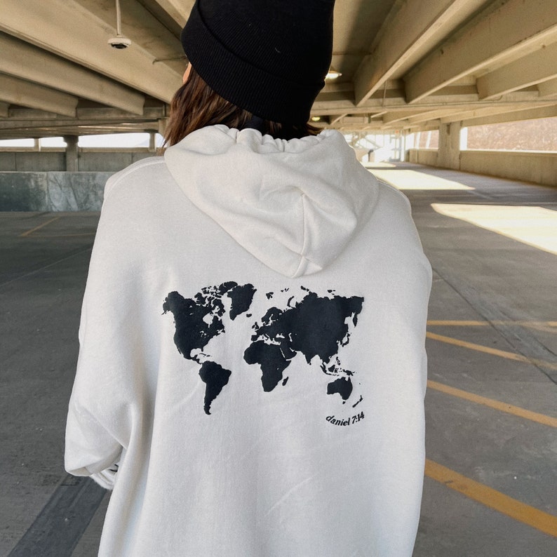 May include: White hoodie with a black world map print on the back. The text "daniel 7:14" is printed below the map.