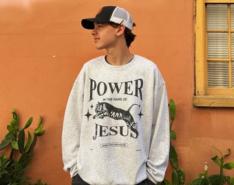 Puede incluir: Una sudadera gris con un gráfico de tigre negro y el texto "POWER IN THE NAME OF JESUS MORE THAN CONQUERORS".
