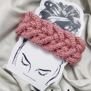 Könnte beinhalten: Ein rosa gestricktes Stirnband mit einem geflochtenen Muster. Das Stirnband liegt auf einer weißen Oberfläche mit einer Zeichnung eines Frauenkopfes und dem Text "Handmade by Crisitina". Der Text "Knitting Pattern" steht unter dem Stirnband.