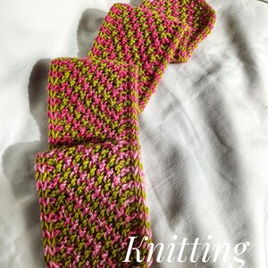 May include: A knitted item in shades of pink and green, possibly a scarf or a similar accessory, is displayed against a white background. The text "Knitting Pattern" is visible in the lower right corner. The item's texture is clearly visible.