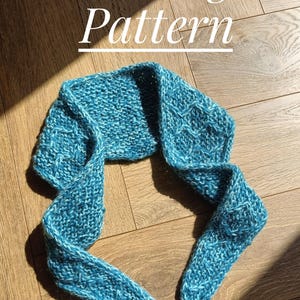 May include: A bright blue knitted scarf featuring a textured diamond pattern throughout the fabric. The text Knitting Pattern is displayed in white letters above the scarf, which has tapered ends and a thick, soft yarn construction.