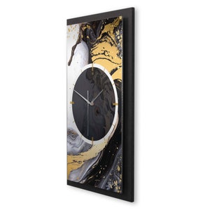 May include: A black and gold abstract wall clock with a white frame. The clock face is black with gold accents and white hands.