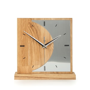 Könnte beinhalten: Eine moderne Holzuhr mit silbernem Zifferblatt und schwarzen Zeigern. Die Uhr hat ein einzigartiges Design mit einem Halbkreis aus Holz und einem Halbkreis aus Silber.