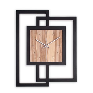 Könnte beinhalten: Eine moderne Wanduhr mit quadratischem Holzgesicht und silbernen Zeigern. Die Uhr ist in einem schwarzen geometrischen Rahmen eingefasst. Das Holzgesicht hat ein natürliches Holzmaserungsmuster. Das Design der Uhr ist minimalistisch und zeitgemäß.