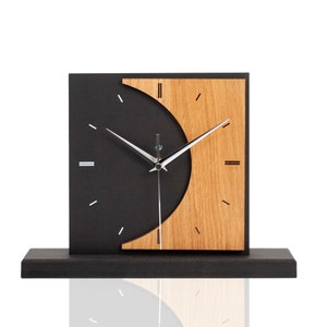Könnte beinhalten: Eine moderne Holzuhr mit schwarzem Zifferblatt und einer Halbkreis aus Holzmaserung. Die Uhr hat silberne Zeiger und schwarze römische Ziffern.