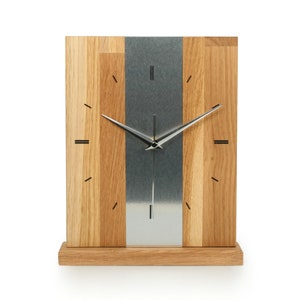 Könnte beinhalten: Eine moderne Holz- und Metalluhr mit silbernem Zifferblatt und schwarzen Zeigern. Die Uhr hat eine rechteckige Form und ist aus hellem Holz mit einer dunkleren Holzleiste gefertigt.