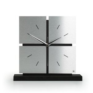 Könnte beinhalten: Eine silberne Uhr mit schwarzen Zeigern und einem schwarzen Sockel. Das Zifferblatt der Uhr ist in vier Abschnitte unterteilt.