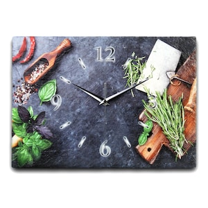 Könnte beinhalten: Eine Schieferuhr mit schwarzem Hintergrund und silbernen Zeigern. Das Zifferblatt der Uhr hat römische Ziffern und ist von verschiedenen Kräutern, Gewürzen und Küchenutensilien umgeben.