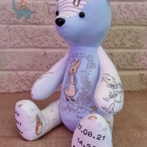 May include: A blue and white Peter Rabbit themed teddy bear with embroidered details. The bear's foot is embroidered with the date 27.06.21, 14.32, and 420 grams.