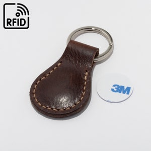 May include: A brown leather key fob with a silver key ring. The fob has a stitched edge and the text "RFID" is printed on a small tag attached to the ring.