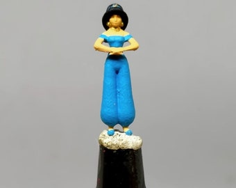 May include: A small blue figurine of a woman wearing a blue turban and blue pants. The figurine is standing on a small white base.