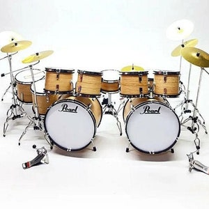May include: A miniature drum set with natural wood-tone drums and shiny silver hardware. The set includes a bass drum, snare, toms, cymbals, and a Pearl logo on the bass drum. The drum set is a miniature replica.