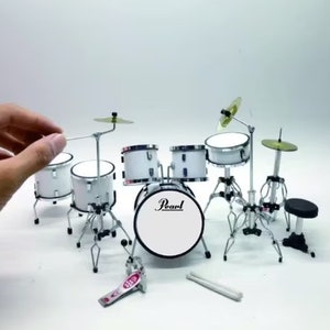 Op de afbeelding: Een witte Pearl drumset met een basdrum, een snare drum, twee toms en een bekken. De drumset staat op een wit oppervlak.