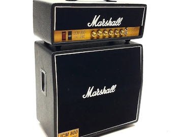 May include: Black Marshall JCM 800 Lead Series guitar amplifier with a black speaker cabinet. The amplifier has a gold nameplate with the text "Marshall" and "JCM 800 Lead Series". The speaker cabinet has a gold nameplate with the text "Marshall" and "JCM 800 Lead - 1960".