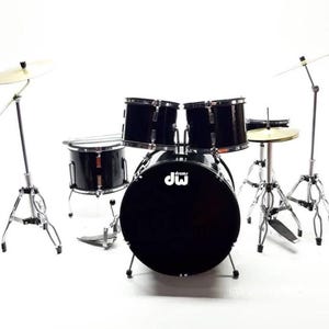 May include: A black drum set with silver hardware. The set includes a bass drum, two mounted toms, a floor tom, a snare drum, and cymbals. The bass drum has the letters "dw" printed on it. The set is on a white background.