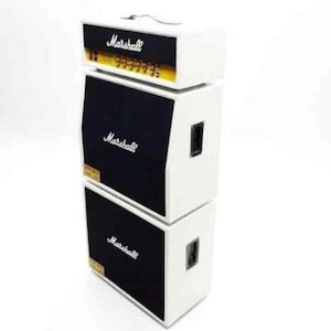 Könnte beinhalten: Ein weißer Marshall-Gitarrenverstärker-Stack mit drei separaten Einheiten. Die obere Einheit hat einen goldenen Grill und den Text "Marshall" in Schwarz. Die mittleren und unteren Einheiten haben schwarze Lautsprechergitter und den Text "Marshall" in Weiß.
