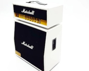 May include: A white Marshall guitar amplifier with a black speaker cabinet. The amplifier has a black faceplate with the word "Marshall" in white lettering. The speaker cabinet has a black faceplate with the word "Marshall" in white lettering and the text "JCM 800 100W 220V" in gold lettering.