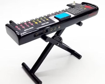 May include: A black toy keyboard with a stand. The keyboard has a series of buttons and keys in various colors, including pink, yellow, and blue. The word "RHYTHM" is visible on the left side of the keyboard. The keyboard is supported by a black, foldable stand.