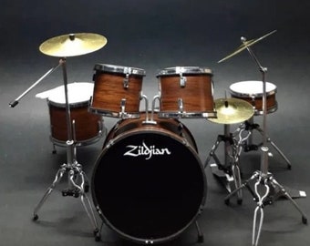 May include: A miniature drum set with a brown wood finish. The set includes a bass drum with a Zildjian logo, a snare drum, two toms, and two cymbals. The drums are mounted on stands.