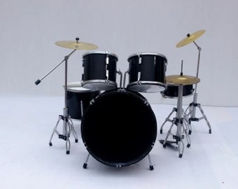 May include: Miniature black drum set with silver hardware and gold-colored cymbals. The set includes a bass drum, snare drum, two tom-toms, and a hi-hat cymbal. The drum set is a toy or decorative item.
