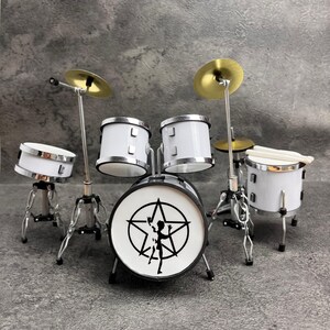 May include: Miniature white drum set with silver accents and gold cymbals. The bass drum features a black and white graphic. Includes drumsticks. A detailed replica of a drum kit.