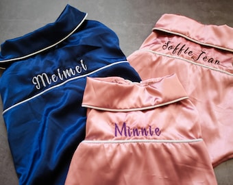 May include: Three personalized satin pajamas in blue, pink, and pink. The pajamas have white piping and are embroidered with the names "Meimei", "Soffie Jean", and "Minnie".