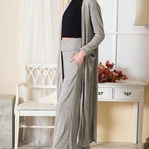 May include: A gray ribbed knit cardigan with long sleeves and pockets, paired with matching wide-leg pants. The outfit is completed with black heeled ankle boots.
