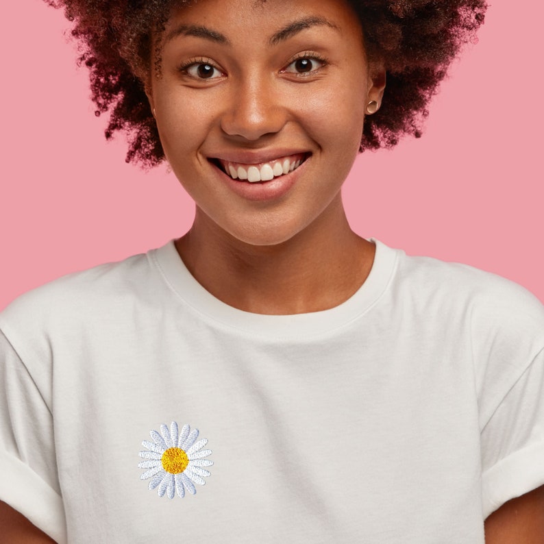 May include: A white t-shirt with a white daisy embroidered on the front. The daisy has a yellow center.