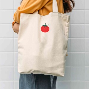May include: A white canvas tote bag with a red embroidered tomato on the front.