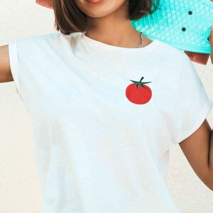 May include: White t-shirt with a red embroidered tomato on the front.
