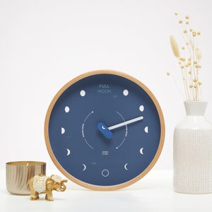 Può includere: Un orologio blu e in legno con sfondo bianco e le parole "FULL MOON" sul quadrante. L'orologio ha una lancetta blu e un cerchio bianco al centro.