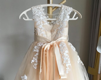 May include: A peach tulle dress with white lace detailing and a satin sash. The dress has a scoop neckline and sleeveless design.