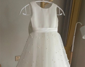 May include: White tulle dress with a satin bodice and pearl embellishments. The dress has a scoop neckline and a sleeveless design. The skirt is full and flowing.