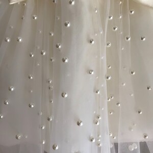May include: A white tulle skirt with a satin bow and pearl embellishments.