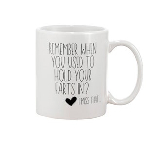 May include: A white ceramic mug with a handle on the right side. The mug features black text that reads: REMEMBER WHEN YOU USED TO HOLD YOUR FARTS IN? followed by a small black heart icon and the text: I MISS THAT...