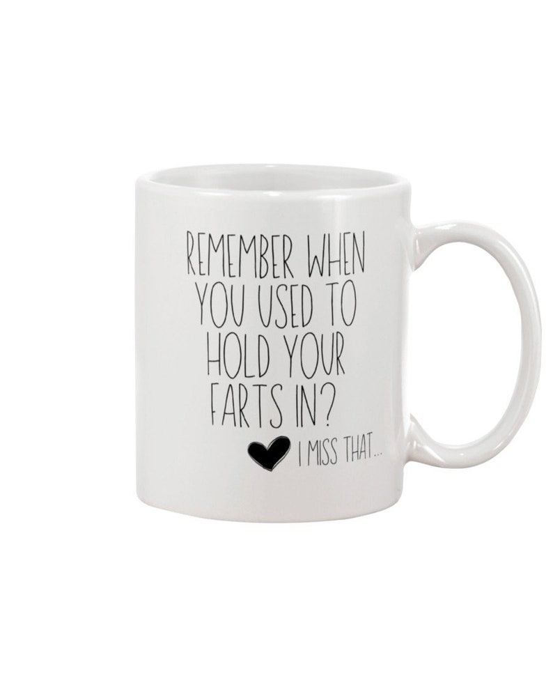May include: A white ceramic mug with a handle on the right side. The mug features black text that reads: REMEMBER WHEN YOU USED TO HOLD YOUR FARTS IN? followed by a small black heart icon and the text: I MISS THAT...