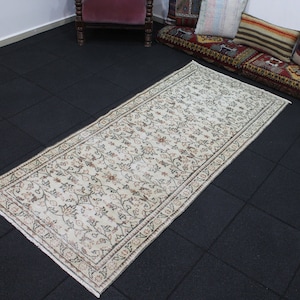以下が含まれることがあります： 白地に茶色とベージュの色の花柄が施されたランナーラグ。ラグは、繰り返しのパターンで縁取られています。