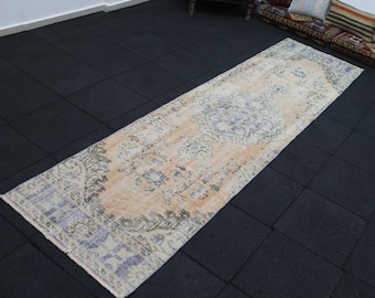 May include: A vintage runner rug with a faded floral pattern in shades of peach, blue, and white. The rug is laid out on a black tiled floor.