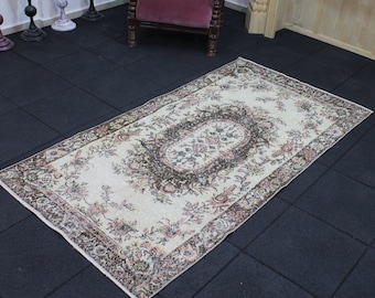 May include: A vintage cream-colored rug with a floral pattern in shades of pink, brown, and white. The rug has a central oval medallion with a floral design and a border with a repeating floral motif.