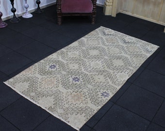 May include: A cream-colored rug with a geometric pattern in shades of gray and purple. The rug has a diamond-shaped design with a central star motif. The rug is laid out on a black tiled floor.