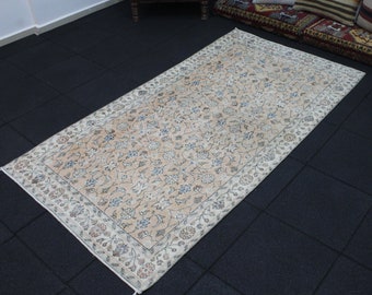 May include: A cream-colored rug with a floral pattern. The rug has a white border and is laid out on a black tiled floor.