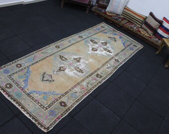 May include: A vintage beige runner rug with a floral pattern in shades of blue, pink, and brown. The rug has a fringed edge and is laid out on a black tiled floor.