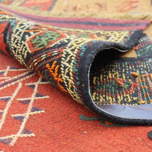 May include: A close-up of a colorful rug with intricate patterns. The rug is folded in half, revealing the underside, which is a dark brown fabric.