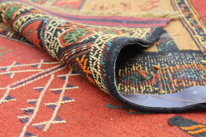 May include: A close-up of a colorful rug with intricate patterns. The rug is folded in half, revealing the underside, which is a dark brown fabric.